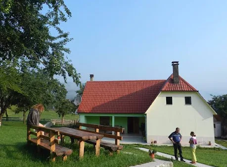 Ndërtesa e bujtinës me çati të kuqe dhe stola druri në livadh